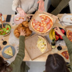 "Mesa repleta de comida variada en una reunión social, con opciones sin gluten y sin alérgenos, como pan, pasteles y aperitivos saludables.