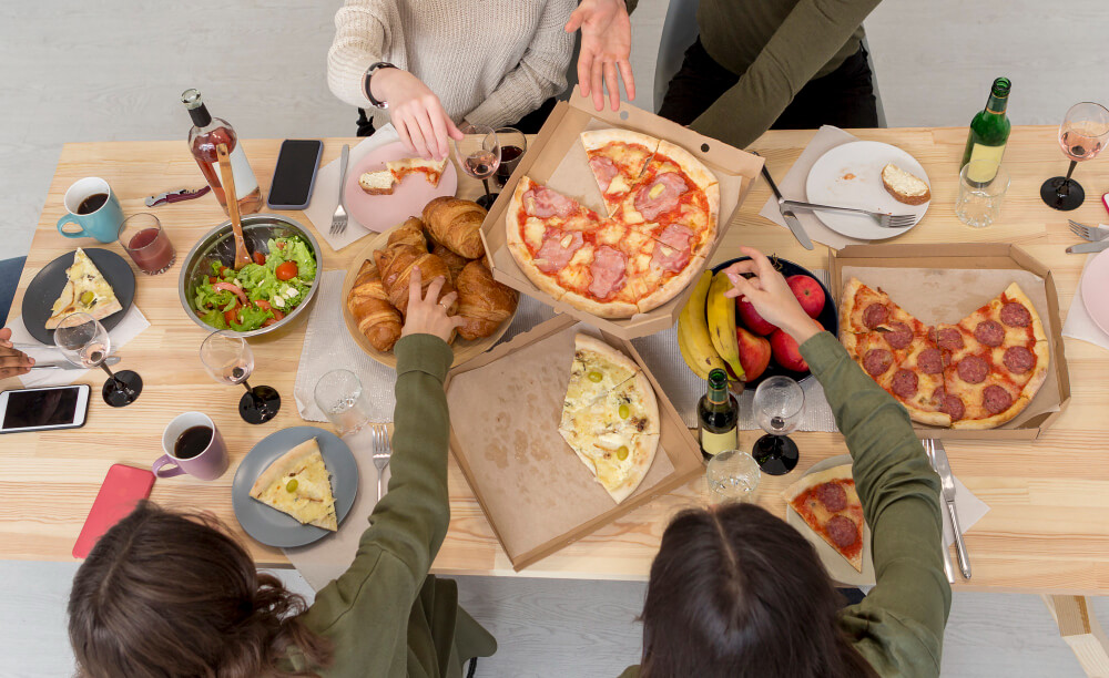 "Mesa repleta de comida variada en una reunión social, con opciones sin gluten y sin alérgenos, como pan, pasteles y aperitivos saludables.