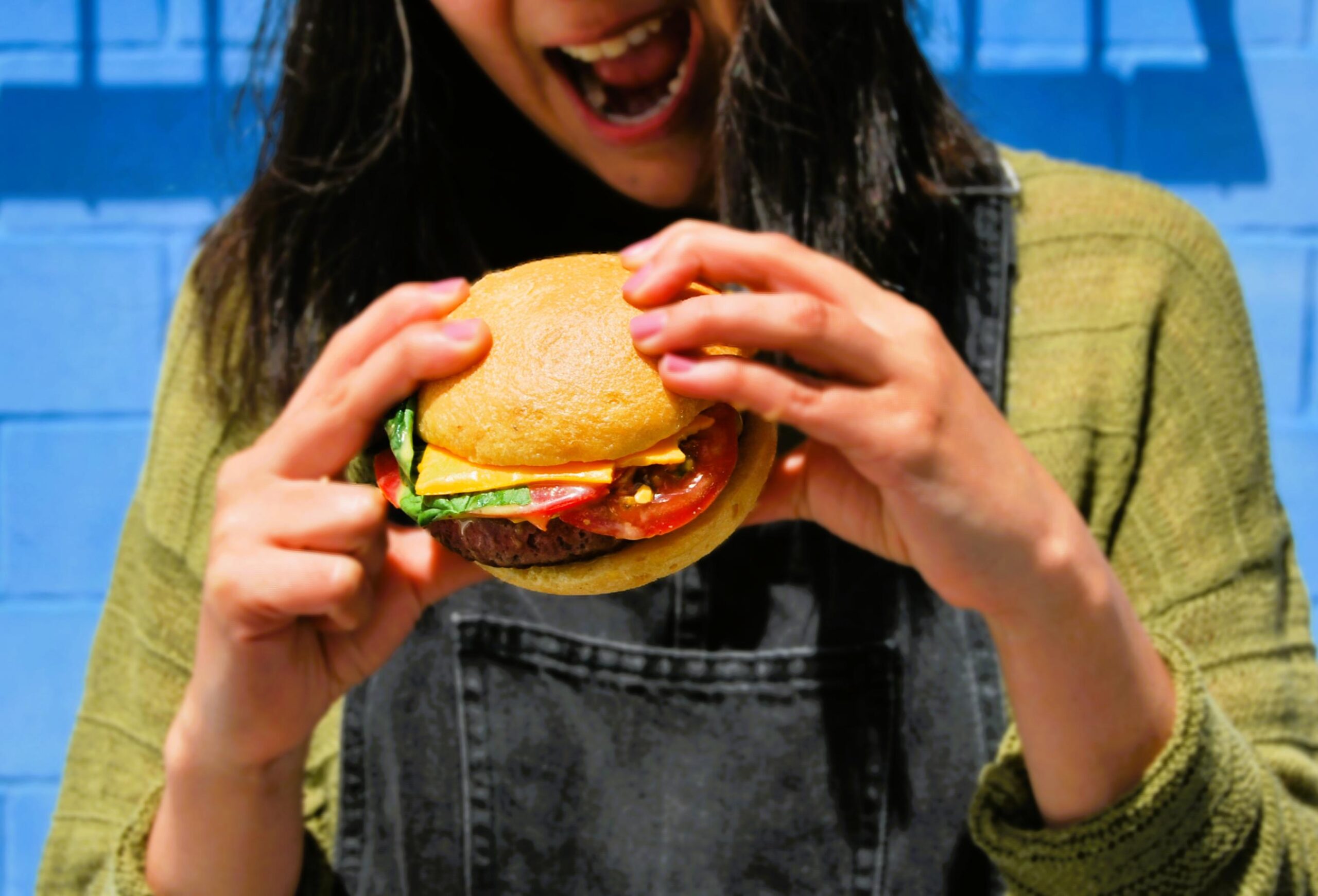 Chica comiendo una hanburguesa de carne con lechuga, tomate y queso