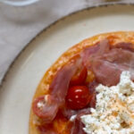 Pizza sin gluten emplatada con burrata, jamón serrano y tomates cherry sobre base Adpan