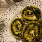 Espirales de hojaldre sin gluten con espinacas, queso feta y parmesano recién horneadas sobre una bandeja.