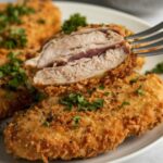 Plato de pollo rebozado crujiente con un tenedor levantando un trozo donde se aprecia el rebozado adherido.