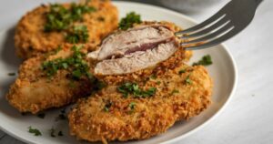 Plato de pollo rebozado crujiente con un tenedor levantando un trozo donde se aprecia el rebozado adherido.