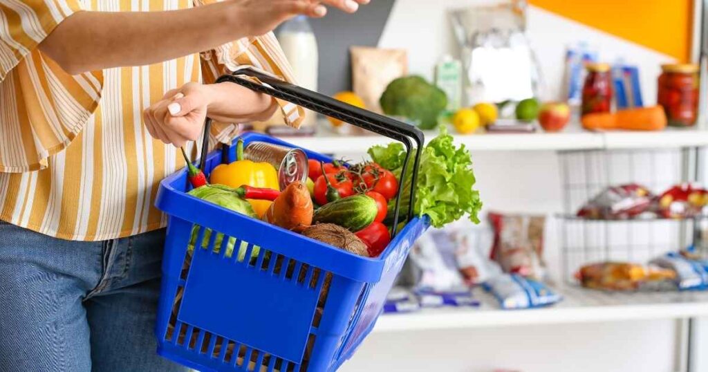 Persona sosteniendo una cesta de la compra azul con verduras frescas y alimentos saludables para una compra sin gluten