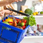 Persona sosteniendo una cesta de la compra azul con verduras frescas y alimentos saludables para una compra sin gluten