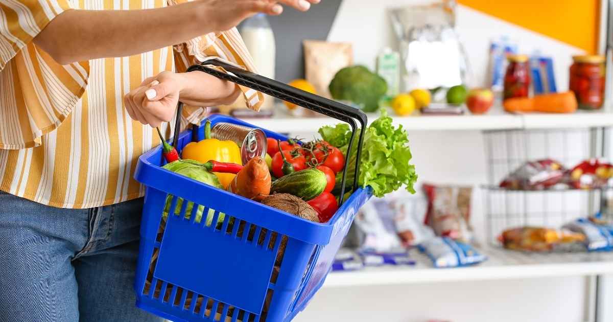 Persona sosteniendo una cesta de la compra azul con verduras frescas y alimentos saludables para una compra sin gluten